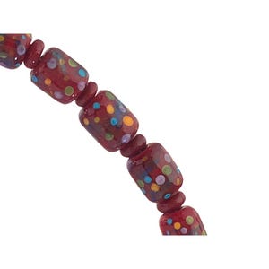 Pode incluir: Um colar composto por contas cilíndricas vermelhas decoradas com pequenos pontos multicoloridos em tons de azul, amarelo e roxo, separadas por contas espaçadoras esféricas menores de cor vermelho escuro sólido num padrão repetitivo.