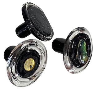 May include: Three glass bottle stoppers with black and clear glass designs. The stoppers have a round top and a cylindrical base.