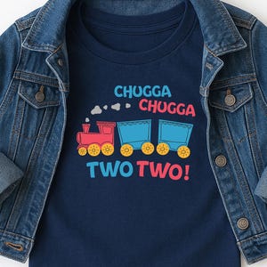 May include: A navy blue t-shirt with a colorful train graphic and the words "CHUGGA CHUGGA TWO TWO!" is layered under a denim jacket. The train is red and blue with yellow wheels. The jacket is a classic denim style.