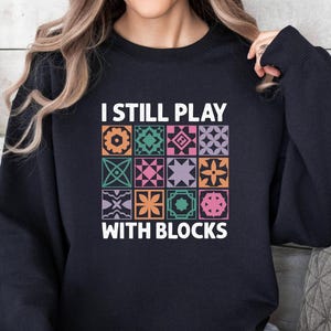 May include: Black sweatshirt with the text "I still play with blocks" and a colorful patchwork design.