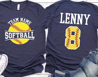 May include: Two navy blue softball t-shirts. One shirt features a yellow softball graphic with the text "Team Name Softball". The other shirt has the name "Lenny" and the number "8" in a softball design.