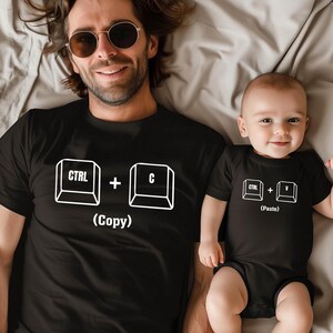 May include: Black t-shirts and onesie with white graphic keyboard symbols. The adult shirt displays "CTRL + C (Copy)", while the baby's onesie shows "CTRL + V (Paste)". The matching outfits are a fun, tech-themed set.