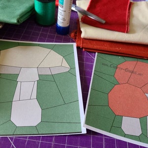 Può includere: Due modelli di carta per un progetto di trapunta patchwork a forma di fungo. I modelli sono stampati su carta bianca con linee nere e sono circondati da uno sfondo verde. I modelli sono etichettati con il sito web "www.Crafty-Geeks.net".