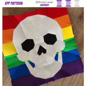 May include: A patchwork textile with a skull motif, set against a rainbow gradient. The skull is white with black eye sockets and a detailed jawline. The text "EPP PATTERN" and "Difficulty Level: MODERATE" are visible. The difficulty level is indicated by three spools.