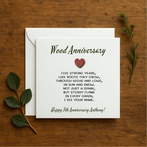 Peut inclure: Une carte blanche avec un cœur vert et le texte "Wood Anniversary" en vert. La carte contient un poème sur cinq ans de mariage et le texte "Happy 5th Anniversary Anthony!"