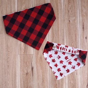 Könnte beinhalten: Zwei Hunde-Bandanas. Eines ist rot und schwarz kariert. Das andere ist weiß mit roten Ahornblättern und dem Wort "CANADA". Beide liegen auf einer Holzoberfläche.