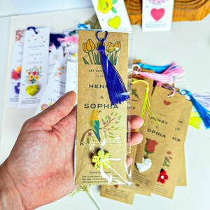 A collection of personalized bookmarks. The bookmarks are brown with printed text and illustrations. One bookmark features a blue tassel and a yellow flower. The text on the bookmarks includes names like Henry and Sophia, and phrases like 'Let Love'. Other bookmarks have heart and flower designs.