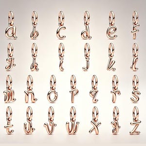 May include: A collection of twenty-six rose gold-toned metal letter charms, each featuring a cursive lowercase alphabet character suspended from a circular jump ring. Many of the letters are accented with a single small, clear, round gemstone.