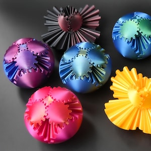 May include: An assortment of colorful, metallic decorative spheres and fan-shaped ornaments. The spheres feature gear-like designs and are in shades of pink, blue, and purple. The fan-shaped ornaments are in yellow and dark gray.