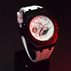 Peut inclure: Une montre-bracelet blanche et noire avec un cadran rouge et blanc. La montre a un bracelet en silicone blanc et un boîtier en métal noir. Le cadran de la montre présente un motif de fleurs de cerisier et le texte "WR 20BAR".