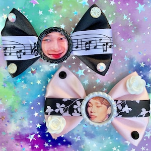 May include: Two handmade hair bows with a black and white musical note ribbon and a pink bow with a black and white floral ribbon. Each bow features a round button with a photo of a person's face.