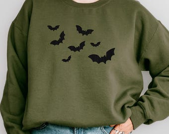 May include: Olive green sweatshirt featuring a black bat graphic. The bats are in various sizes and positions, creating a dynamic design. The long-sleeved top is made of a soft material, perfect for casual wear.