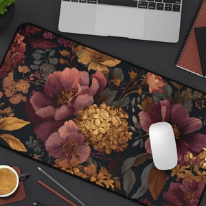 May include: A floral desk mat featuring a dark background with burgundy, gold, and peach-colored flowers. The mat has a black border and is shown with a laptop, mouse, pens, and a coffee cup.