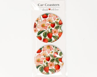 May include: Two round car coasters with a floral pattern featuring pink flowers and red strawberries on a white background. The coasters are packaged in a clear plastic sleeve with a price tag that reads "$9.50". The text "Car Coasters" and "Handmade with love" is printed on the packaging.