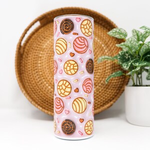 May include: A pink stainless steel tumbler with a pattern of colorful pastries, including conchas, on the exterior.