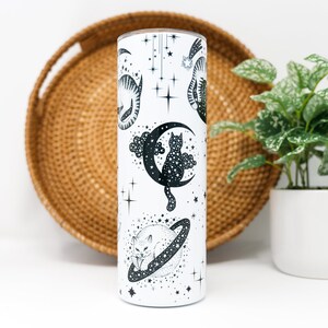 May include: White stainless steel tumbler with a black and white design of cats and stars. The tumbler has a black lid.