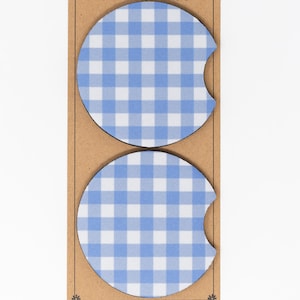 May include: Two blue and white gingham patterned beverage coasters. The coasters are round with a cut-out for a cup handle.