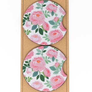May include: Two round pink and green floral patterned coasters. The coasters are made of a cork-like material and have a cut-out for a cup.
