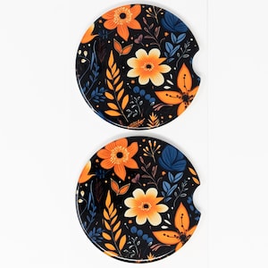 May include: Two round black car coasters with a floral pattern. The pattern features orange, yellow, and blue flowers and leaves.