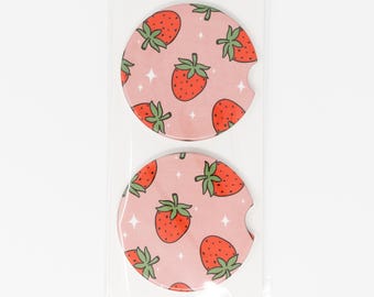 May include: Two pink round coasters with a white background and a repeating pattern of red strawberries with green leaves.