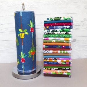 A stack of 20 mixed plant pattern and color reusable paper towels next to a retro hanging plant pattern on a paper towel roll.  Patterns include floral, leaf, plant, and retro design with 10 different earthy solid colors.