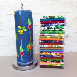 A stack of 20 mixed plant pattern and color reusable paper towels next to a retro hanging plant pattern on a paper towel roll.  Patterns include floral, leaf, plant, and retro design with 10 different earthy solid colors.