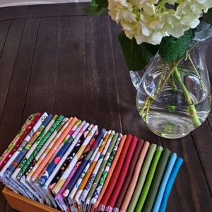 A table with a vase of hydrangea.  Next to it is a bamboo box with folded brightly colored and patterned napkins.  Each napkin edge is visible creating a rainbow effect.