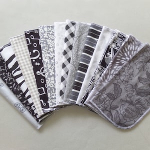 May include: A collection of 16 black and white fabric squares with various patterns, including floral, geometric, and musical notes. The squares are arranged in a fan shape.