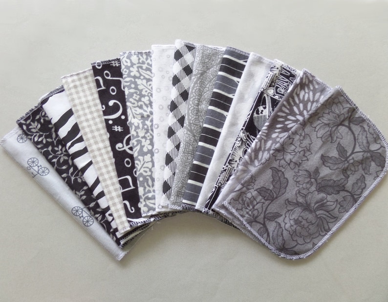 May include: A collection of 16 black and white fabric squares with various patterns, including floral, geometric, and musical notes. The squares are arranged in a fan shape.