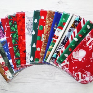 May include: A set of 16 Christmas-themed fabric squares with various designs, including Santa Claus, reindeer, snowmen, and Christmas trees. The squares are arranged in a fan shape on a white wooden surface.