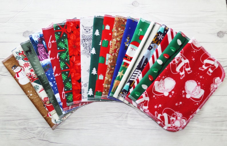 May include: A set of 16 Christmas-themed fabric squares with various designs, including Santa Claus, reindeer, snowmen, and Christmas trees. The squares are arranged in a fan shape on a white wooden surface.