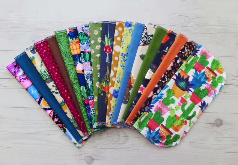 A fan of brightly colored unpaper towels.   Each pattern is different featuring a variety of houseplant, cacti, floral, fruit and retro patterns. Solid colors include teal, brown, oxford blue, olive green and orange.