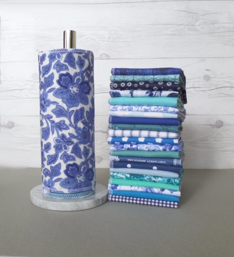 A stack of 20 mixed blue pattern and color reusable paper towels  next to an elegant blue floral Chinoiserie pattern on a paper towel roll.  Patterns include floral, stripe, dot, gingham, whimsical print.  Solid colors include 10 different blue hues.