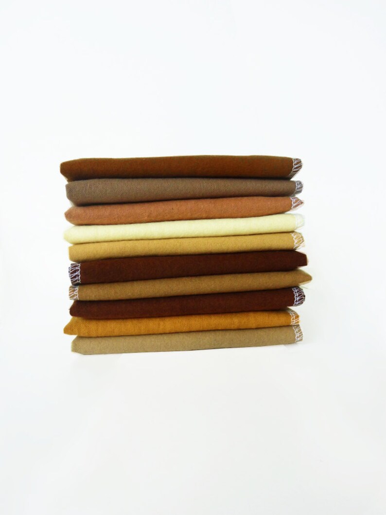 May include: A stack of folded fabric in various shades of brown and tan. The fabrics are neatly arranged, with visible edges and a textured appearance. The edges of the fabric have a decorative trim. The overall aesthetic is simple and clean.