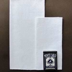 May include: Two white cotton handkerchiefs, one larger than the other, are laid out on a brown surface. A deck of blue and white Monte Carlo Jumbo Playing Cards is placed on top of the smaller handkerchief.