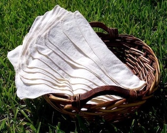 May include: A wicker basket filled with a stack of white cloth baby wipes. The basket is sitting on a bed of green grass.