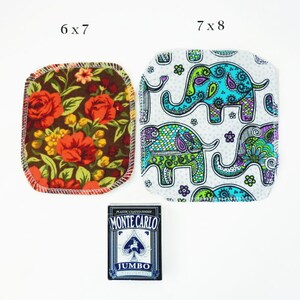 Puede incluir: Dos cuadrados de tela con diferentes patrones. El primer cuadrado mide 6x7 pulgadas y presenta un patr&oacute;n floral con flores rojas, naranjas y amarillas sobre un fondo marr&oacute;n. El segundo cuadrado mide 7x8 pulgadas y presenta un fondo blanco con un patr&oacute;n repetido de elefantes coloridos. Una baraja de cartas se encuentra en el centro de la imagen.