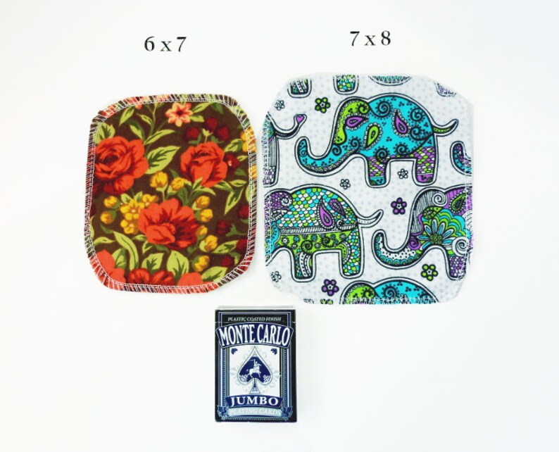 Puede incluir: Dos cuadrados de tela con diferentes patrones. El primer cuadrado mide 6x7 pulgadas y presenta un patr&oacute;n floral con flores rojas, naranjas y amarillas sobre un fondo marr&oacute;n. El segundo cuadrado mide 7x8 pulgadas y presenta un fondo blanco con un patr&oacute;n repetido de elefantes coloridos. Una baraja de cartas se encuentra en el centro de la imagen.