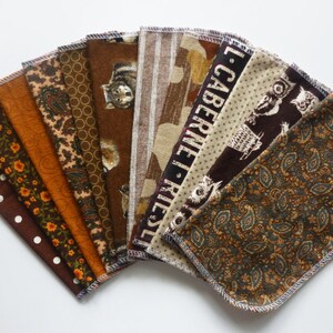 May include: A collection of ten fabric squares with various patterns, including polka dots, floral, paisley, and owl designs. The color palette consists of browns, oranges, and tans. Each square has a stitched edge.