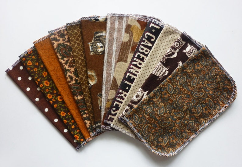 May include: A collection of ten fabric squares with various patterns, including polka dots, floral, paisley, and owl designs. The color palette consists of browns, oranges, and tans. Each square has a stitched edge.