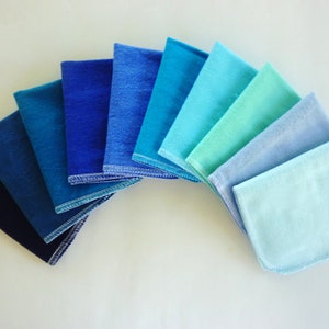 A fan shape of 10 paperless  towels in an ombre of blue solid colors from dark to light.  Navy, midnight blue, dark teal, royal blue, oxford blue, powder blue, electric blue, aqua, light blue, baby blue.