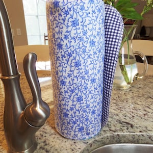 A roll of blue pattern unpaper towels next to a kitchen sink.  The main pattern is a tiny blue floral on white background.  The towel ready to be pulled off is a navy blue gingham.