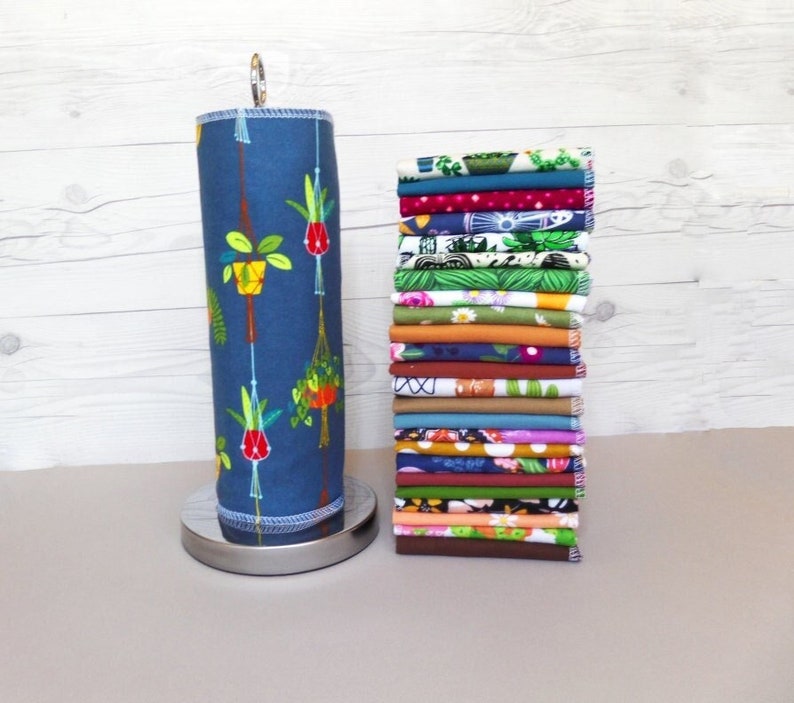 A stack of 20 mixed plant pattern and color reusable paper towels next to a retro hanging plant pattern on a paper towel roll.  Patterns include floral, leaf, plant, and retro design with 10 different earthy solid colors.