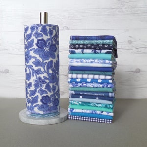 A stack of 20 mixed blue pattern and color reusable paper towels next to an elegant blue floral Chinoiserie pattern on a paper towel roll.  Patterns include floral, stripe, dot, gingham, whimsical print.  Solid colors include 10 different blue hues.