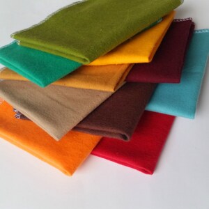 May include: A stack of eight fabric squares in various colors, including orange, yellow, green, brown, red, and blue. The fabric squares are folded and stacked on top of each other.