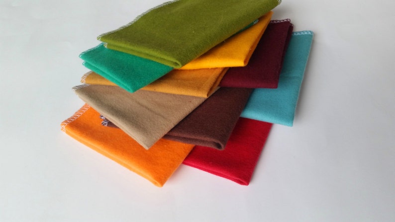 May include: A stack of eight fabric squares in various colors, including orange, yellow, green, brown, red, and blue. The fabric squares are folded and stacked on top of each other.