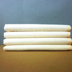 May include: A stack of five white cotton dishcloths with orange stitching around the edges.