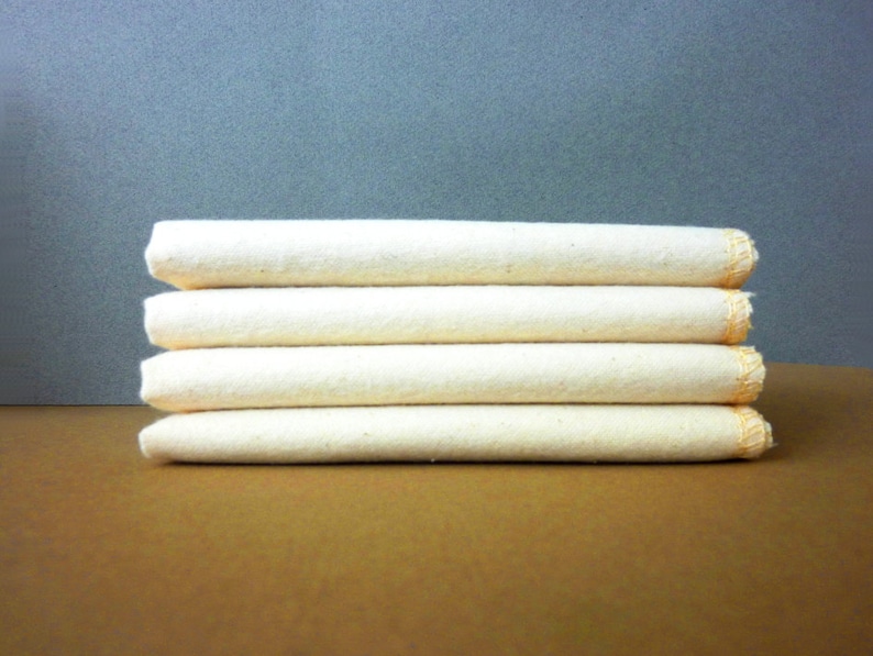 May include: A stack of five white cotton dishcloths with orange stitching around the edges.