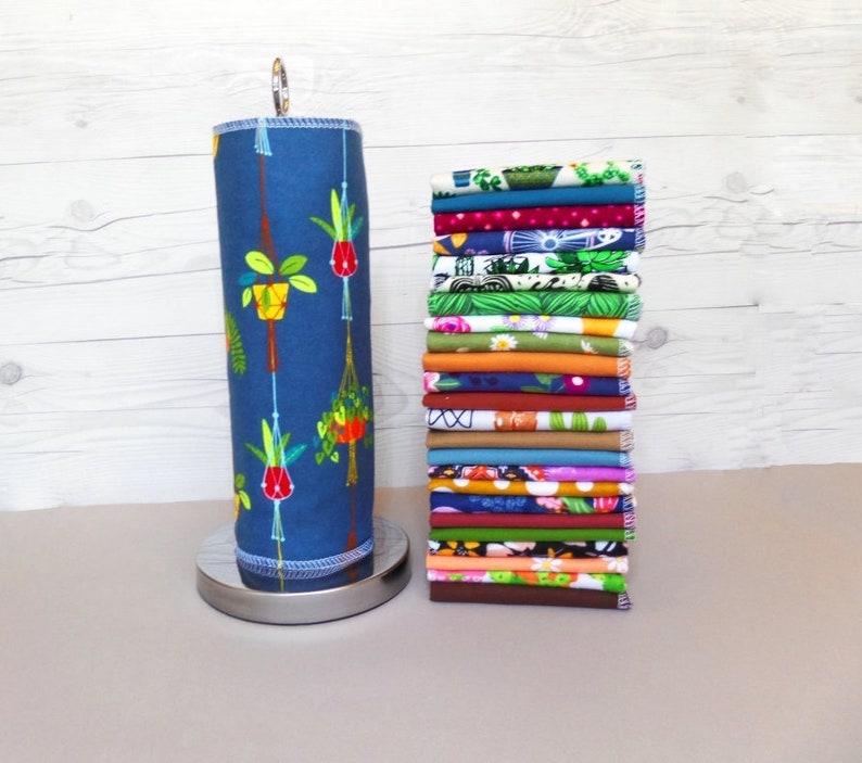 A stack of 20 mixed plant pattern and color reusable paper towels next to a retro hanging plant pattern on a paper towel roll.  Patterns include floral, leaf, plant, and retro design with 10 different earthy solid colors.