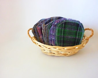 Puede incluir: Una cesta de mimbre llena de una pila de almohadillas de desmaquillaje reutilizables hechas de tela a cuadros en tonos verdes, morados y azules.